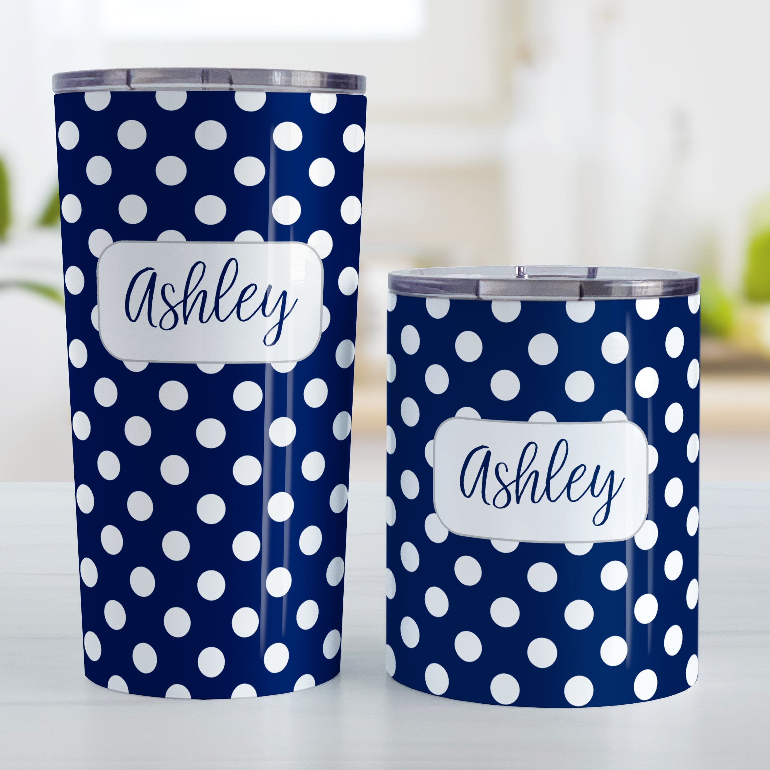 Personalized Dark Blue Polka Dot Tumbler Cup (20oz and 10oz, stainless steel insulated) at Amy's Coffee Mugs. These cups are designed with a pattern of white polka dots over a dark navy blue background color that wraps around the cups. Your name is personalized in a dark blue script font over the polka dot pattern. Photo shows both sized cups on a table next to each other. 